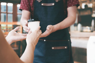 Midsection of waiter giving coffee cup to woman at cafe