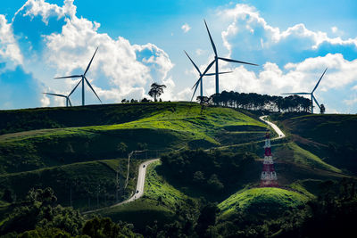 Low angle view of windmills on hills against cloudy sky during sunny day