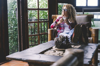 Woman drinking coffee while sitting on sofa by window