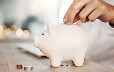 Midsection of man putting coin in piggy bank