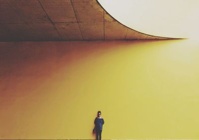 Rear view of woman standing against yellow wall