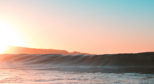 Scenic view of sea and wave peaking against clear sky during sunset