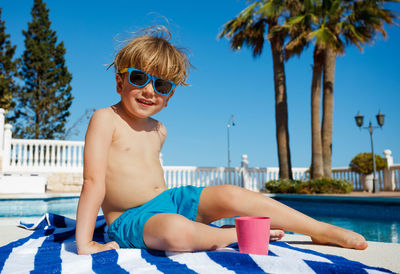 Portrait of woman wearing sunglasses while sitting on bed at beach