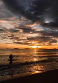 Silhouette woman on beach against sky during sunset