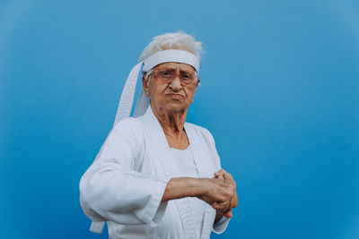 Portrait of senior woman doing karate against blue background