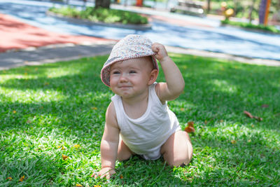 Little baby girl in white clothing and panama. child playing on grass on a sunny summer day.