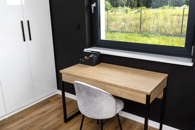 A wooden table with chair under the window in a modern boy room in black and white colors. 