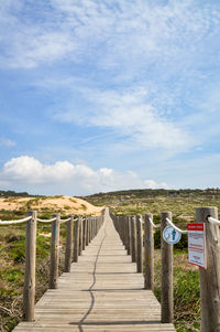 View of empty wooden walkway against cloudy sky