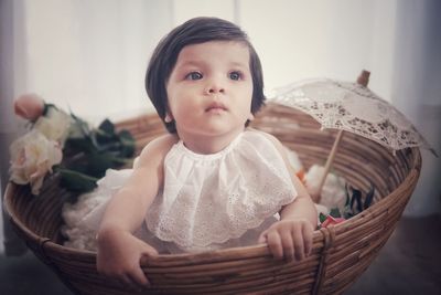 Close-up of cute baby girl looking away while sitting in wicker basket