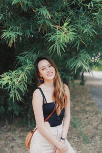 Portrait of smiling young woman standing against plants in park