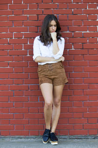 Portrait of young woman standing against brick wall