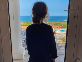 Rear view of woman looking at sea seen through window