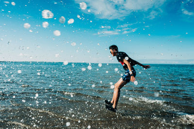 Side view of boy jumping in sea against sky