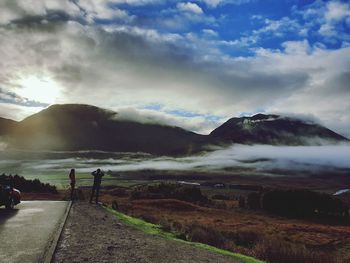 Hikers standing on mountain against sky