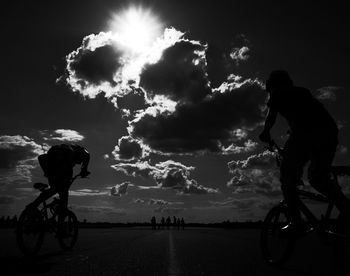 Low angle view of silhouette person riding bicycle against cloudy sky