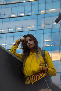 Young woman standing against yellow wall