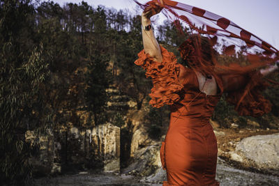 Rear view of woman holding fabric while standing against trees