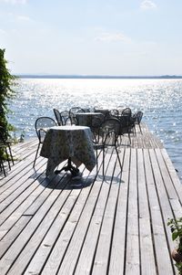 Wooden bench on table by sea against sky