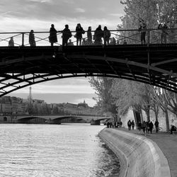 People on footbridge over river against sky