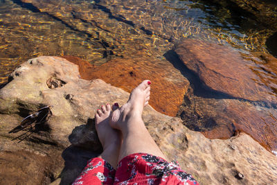 Young girl feet relaxing and sunglasses on rock at the edge of river flowing clear water 