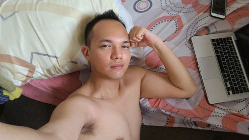 High angle portrait of shirtless young man lying on bed