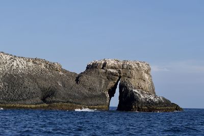 Rock formation by sea against clear sky