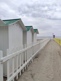 Footpath amidst beach huts against sky