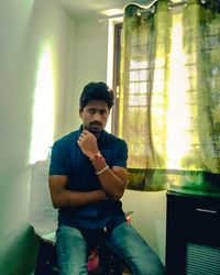Young man looking away while sitting on window at home