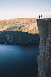 Scenic view of mountain and lake with men on rock against sky