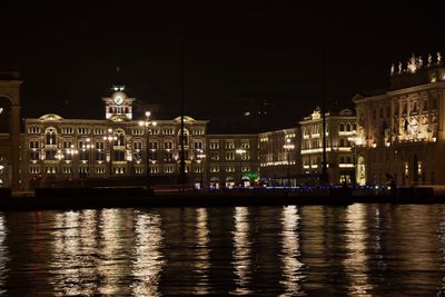 Illuminated buildings by river against sky in city at night