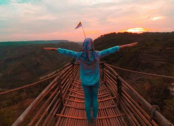 Man standing on railing against sky during sunset