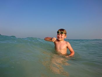 Cute smiling shirtless boy in sea against sky