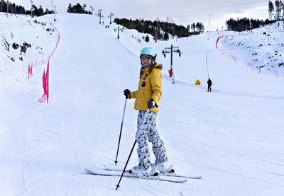 Smiling young woman in yellow jacket ski helmet skiing on mountain slope, winter sports alpine skis