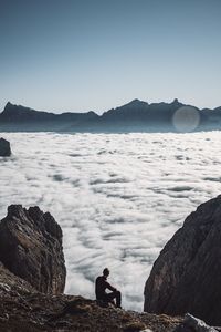 People sitting on rocks by sea against sky