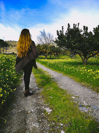 Rear view of woman standing on road amidst plants against sky