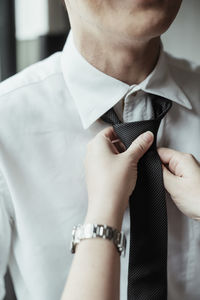 Cropped hand tying tie of man