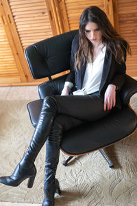 Full length of young woman sitting on chair at home