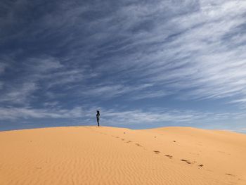 Low angle view of man walking on sand dune in desert against cloudy sky