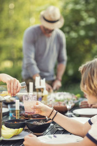 Cropped hand of teenage girl pouring drink in glass held by brother over dining table at back yard