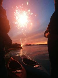 People standing canoes against firework display over river