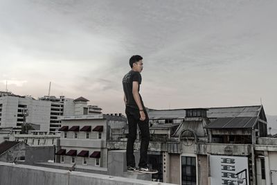 Young man standing on terrace in city against sky