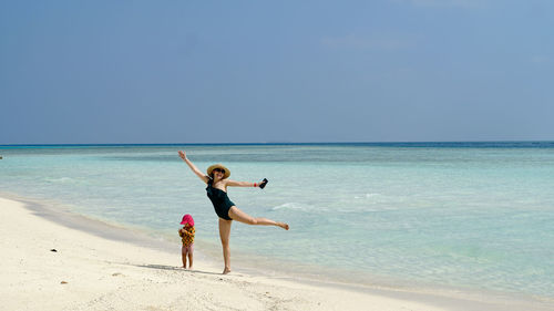 Full length of woman jumping at beach with baby