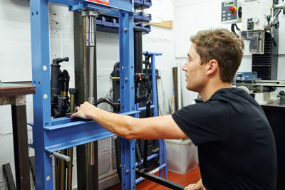 Side view of adult man using hydraulic press while working in modern repair workshop