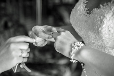 Close-up of bride putting rings in finger with person