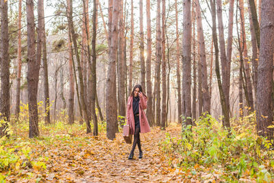 Full length of young woman standing amidst trees in forest