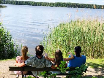 Rear view of people sitting on bench by lake