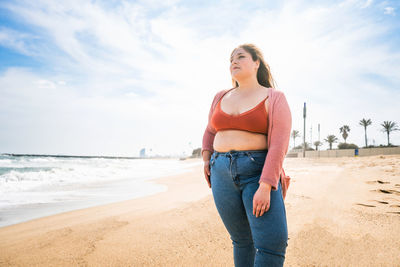 Young woman standing on sand against sky