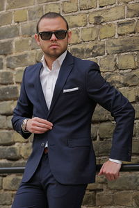 Confident businessman leaning on railing against brick wall