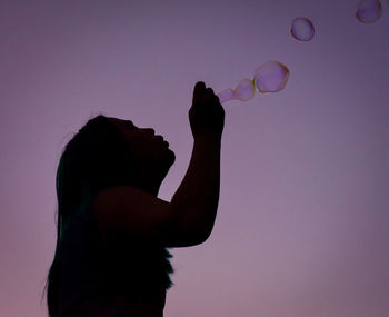 Low angle view of silhouette woman blowing bubbles against clear sky