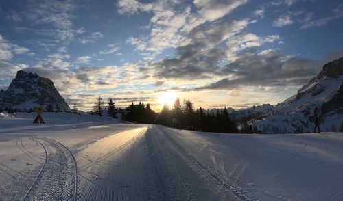 Snow covered road against sky during sunrise